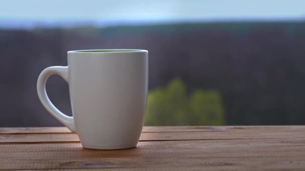 Une tasse de thé chaud ou de café se tient près d'une fenêtre ouverte et émet de la vapeur — Video