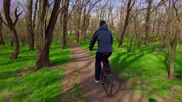 Chico joven monta una bicicleta a lo largo de un camino en un bosque verde, Vista trasera en Slow Mo — Vídeo de stock