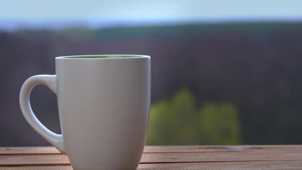 En kopp varmt te eller kaffe står vid ett öppet fönster och sänder ut Steam — Stockvideo