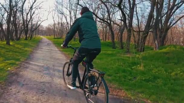 Jonge man rijdt een fiets langs een pad in een groen bos, achter uitzicht in Slow Mo — Stockvideo