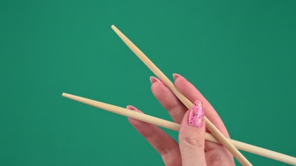 Las manos femeninas sostienen palillos japoneses para rollos de sushi sobre fondo verde — Vídeos de Stock