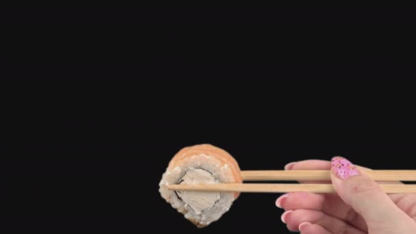 Руки женщин держат японские палочки для еды с суши-роллами на прозрачном фоне — стоковое видео