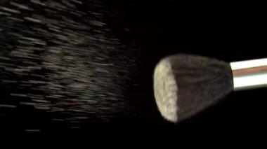 Cosmetic Powder for the Face is Poured from a Brush on a Black Background