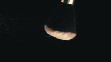 Cosmetic Powder for the Face is Poured from a Brush on a Black Background
