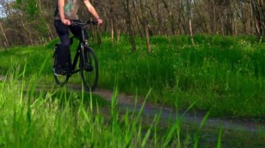 Genç adam gün batımında ormanda tozlu bir patika boyunca bisiklet sürüyor. Ormanda bisiklete binen bir adam sağlıklı bir hayat sürüyor. Spor, eğlence ve hobi, sağlık sigortası, fitness. Seyahat.