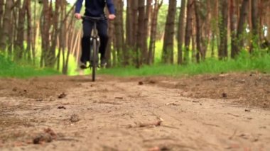 Genç adam gün batımında ormanda tozlu bir patika boyunca bisiklet sürüyor. Ormanda bisiklete binen bir adam sağlıklı bir hayat sürüyor. Spor, eğlence ve hobi, sağlık sigortası, fitness. Seyahat.