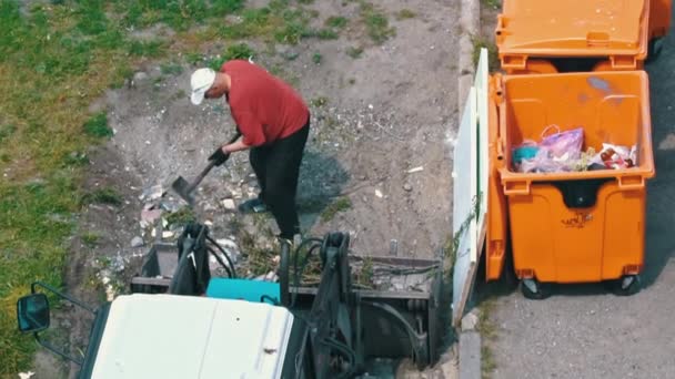 シャベルを持った男はゴミをトラクタータンクに積み込む ゴミ収集車が頑張っている ゴミ缶の近くのゴミ収集 — ストック動画