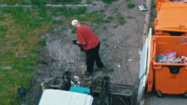 Kürekli bir adam traktör tankına çöp yüklüyor. Çöp kamyonu çok çalışıyor. Çöp tenekelerinin yanında çöp toplama.