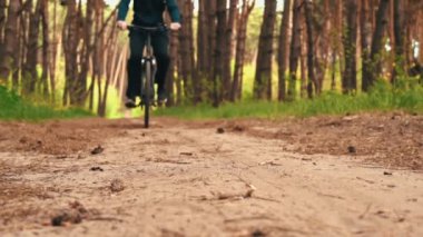 Genç adam gün batımında ormanda tozlu bir patika boyunca bisiklet sürüyor. Ormanda bisiklete binen bir adam sağlıklı bir hayat sürüyor. Spor, eğlence ve hobi, sağlık sigortası, fitness. Seyahat.