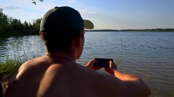 Молодой Человек Кепке Сидит Реки Смартфоне Природе Спокойствие Отдых Уединение — стоковое видео