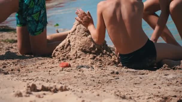 水着の子供たちはビーチで砂の中で遊ぶ 小さな子供たちが海岸に砂の城を構築します 海での子供のエンターテイメント — ストック動画