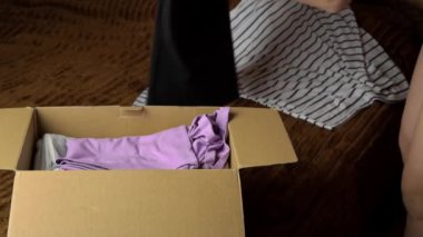 Genç bir kız, içinde eşyalar olan bir paket topluyor ve elbiseleri inceliyor. Kadın güzel şeyleri kahverengi bir kutuya koyar. Nesnelerin internet ve posta yoluyla teslimatı.