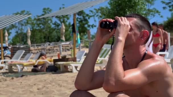 Hombre Playa Traje Baño Está Vigilando Alguien Través Prismáticos Salvavidas — Vídeos de Stock