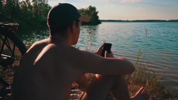 Mladý Muž Čepici Sedí Řeky Chytrém Telefonu Přírodě Klid Odpočinek — Stock video