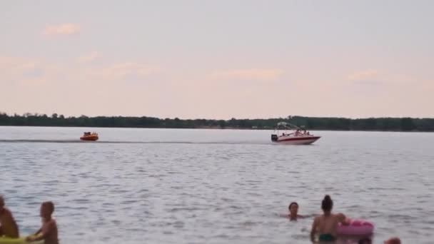 小船沿河漂流 在海滩上系上一根管子 水面上的极端娱乐 船载着人在管子里 — 图库视频影像
