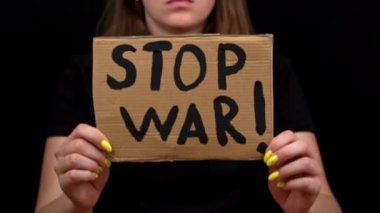 Ukraynalı zavallı kız askeri çatışmayı protesto ediyor. Genç bir kadın, siyah bir arkaplanda savaşı durdurmak için yazıyla sancak kaldırıyor. Kriz dünyası.