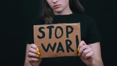 Ukraynalı zavallı kız askeri çatışmayı protesto ediyor. Genç bir kadın, siyah bir arkaplanda savaşı durdurmak için yazıyla sancak kaldırıyor. Kriz dünyası.