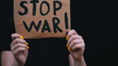 Ukraynalı zavallı kız askeri çatışmayı protesto ediyor. Genç bir kadın, siyah bir arkaplanda savaşı durdurmak için yazıyla sancak kaldırıyor. Kriz dünyası.