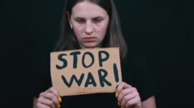 Ukraynalı zavallı kız askeri çatışmayı protesto ediyor. Genç bir kadın, siyah bir arkaplanda savaşı durdurmak için yazıyla sancak kaldırıyor. Kriz dünyası.
