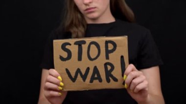 Ukraynalı zavallı kız askeri çatışmayı protesto ediyor. Genç bir kadın, siyah bir arkaplanda savaşı durdurmak için yazıyla sancak kaldırıyor. Kriz dünyası.