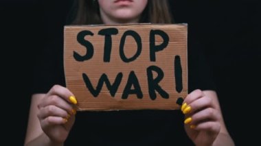 Ukraynalı zavallı kız askeri çatışmayı protesto ediyor. Genç bir kadın, siyah bir arkaplanda savaşı durdurmak için yazıyla sancak kaldırıyor. Kriz dünyası.