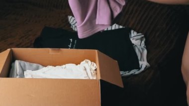 Genç bir kız, içinde eşyalar olan bir paket topluyor ve elbiseleri inceliyor. Kadın güzel şeyleri kahverengi bir kutuya koyar. Nesnelerin internet ve posta yoluyla teslimatı.