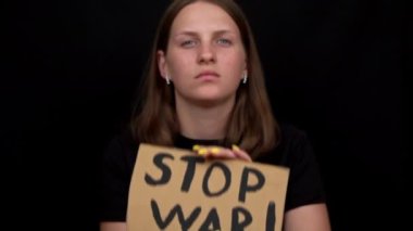 Ukraynalı zavallı kız askeri çatışmayı protesto ediyor. Genç bir kadın, siyah bir arkaplanda savaşı durdurmak için yazıyla sancak kaldırıyor. Kriz dünyası.