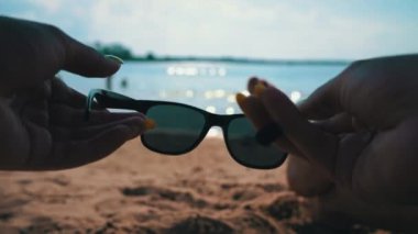 Girl puts on glasses on the sea coast view from the hands. Womens hands put on sunglasses on the background of sea water.