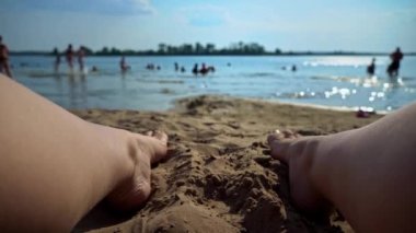 Hands put a milkshake on the background of womens legs and the beach. Marine theme, relaxation. Legs of a girl near a glass with a straw on the background of the sea.