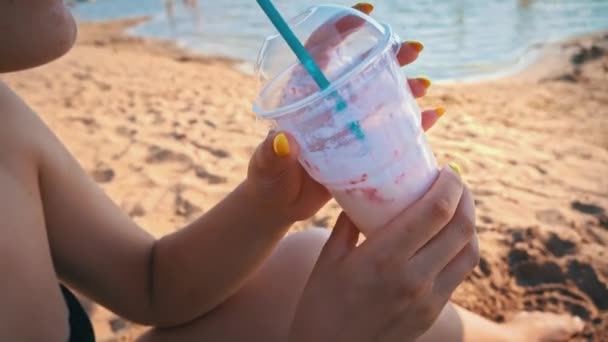 소녀는 해변에서 쉐이크를 마신다 해변에서 모래를 배경으로 칵테일을 마신다 — 비디오