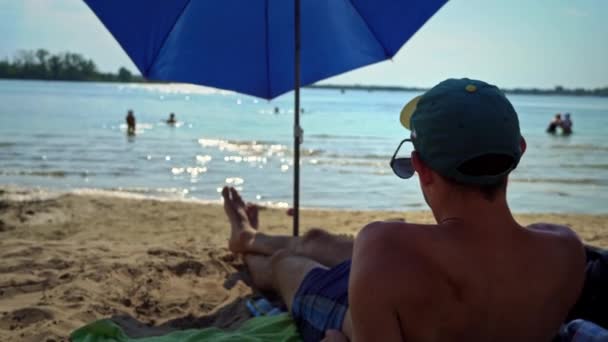 Чоловік Лежить Пляжі Сонячні Ванни Під Парасолькою Світлий День Молодий — стокове відео