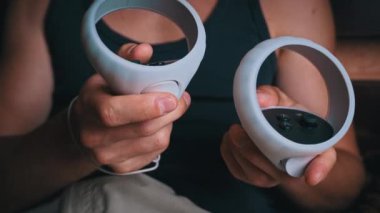 Sanal gerçeklik kasklı bir adam kontrolörleri kontrol eder. Evde yatakta oturan genç bir adam sanal gerçekliktedir. Metaverse. Modern teknolojiler, başka bir dünyaya dalma.