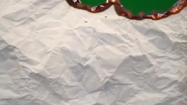White paper burns from above on a green background copy space. The sheet of paper burns and reveals a green background for pasting.