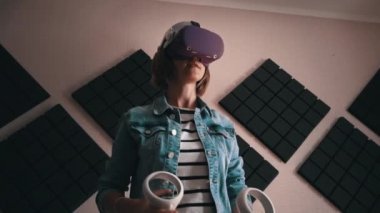 Beautiful girl in a virtual reality helmet with controllers in hands. Active wearing indoor virtual reality simulator while enjoying 3D cyberspace. Augmented reality. Virtual world, new technologies.