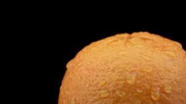 Water drips on an orange orange on a black background in slowmo. Raindrops land on citrus. Water drips from sweet juicy oranges at very close range.