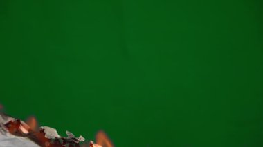 White paper burns from below on a green background copy space. The sheet of paper burns and reveals a green background to insert a reverse footage.