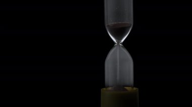 Sand in the hourglass crumbles in the dark. The countdown hourglass is pouring on a black background. Sand falls into a glass flask. Sand is poured onto the flask of the hourglass.