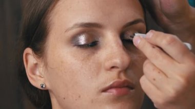 Beautiful girl is put on make-up on her face and glues her eyelashes. Make-up artist paints a young womans face. Womens beauty. Emphasize the natural beauty of the girl.