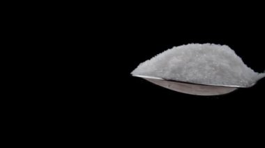 Sugar cubes fall into a teaspoon on a black background in slow motion. White sugar cubes fall on granulated sugar. The sugar spreads evenly. Benefits or harms of consumption for health.
