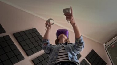 Beautiful girl in a virtual reality helmet with controllers in hands. Active wearing indoor virtual reality simulator while enjoying 3D cyberspace. Augmented reality. Virtual world, new technologies.