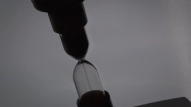Sand in the hourglass crumbles in the dark. The countdown hourglass is pouring on a black background. Sand falls into a glass flask. Sand is poured onto the flask of the hourglass.