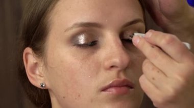 Beautiful girl is put on make-up on her face and glues her eyelashes. Make-up artist paints a young womans face. Womens beauty. Emphasize the natural beauty of the girl.