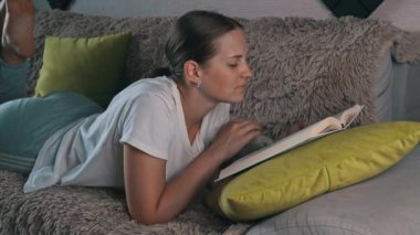 Girl is reading a book at home with her domestic gray cat. Happy lady in casual wear smiling and relaxing at home with her pet. Home leisure concept.