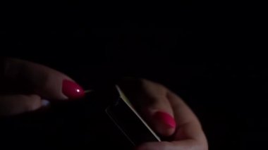 Womens hands light a fire with a match in the dark. The matchbox creates an orange flame. Light from fire. A flickering light in the dark.