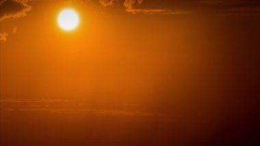 Time lapse bright orange sunset sun sets behind the clouds. The end of the day, the sun goes below the horizon. Big red hot sun in warm air distortion above the horizon.