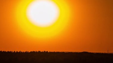 Time lapse bright orange sunset sun sets behind the clouds. The end of the day, the sun goes below the horizon. Big red hot sun in warm air distortion above the horizon.