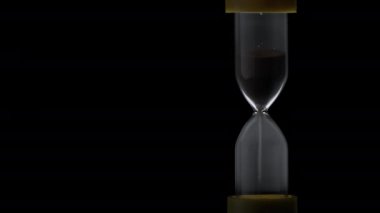 Sand in the hourglass crumbles in the dark. The countdown hourglass is pouring on a black background. Sand falls into a glass flask. Sand is poured onto the flask of the hourglass.