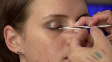 Beautiful girl is put on make-up on her face and glues her eyelashes. Make-up artist paints a young womans face. Womens beauty. Emphasize the natural beauty of the girl.