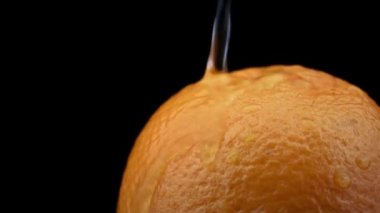 Water drips on an orange orange on a black background in slowmo. Raindrops land on citrus. Water drips from sweet juicy oranges at very close range.