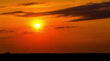 Time lapse bright orange sunset sun sets behind the clouds. The end of the day, the sun goes below the horizon. Big red hot sun in warm air distortion above the horizon.